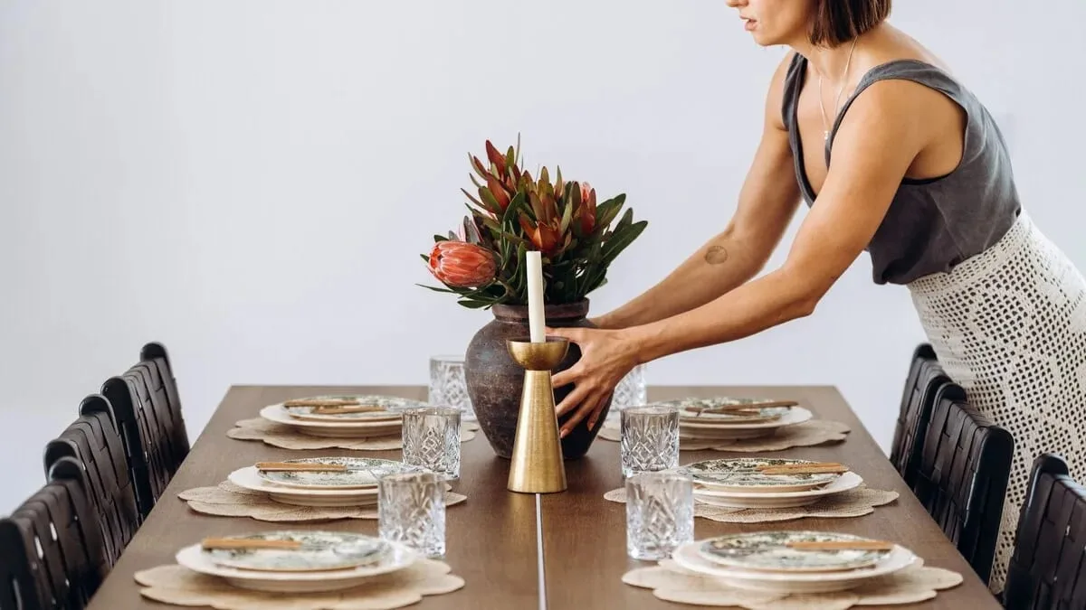 A woman preparing a villa dining table with plates, glasses and flowers