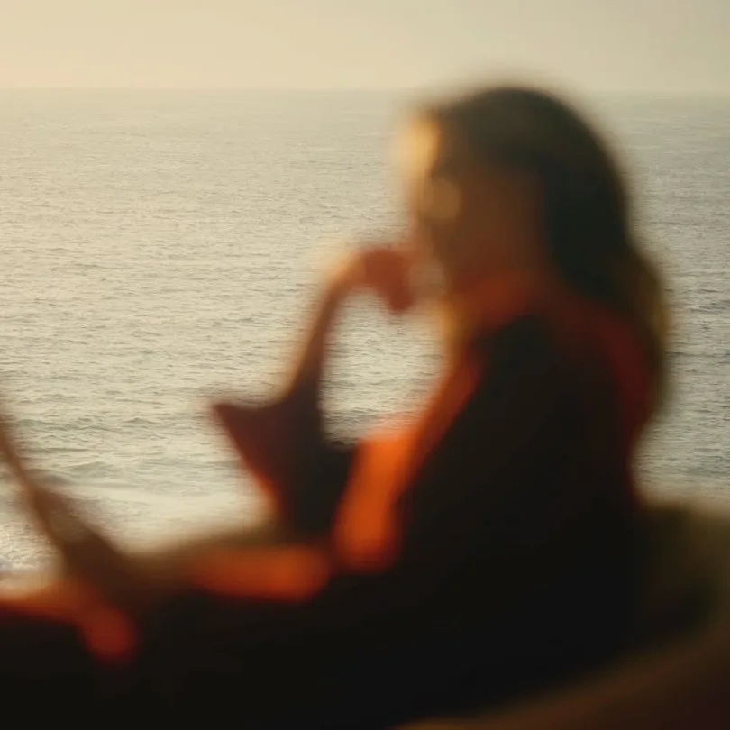 A woman reads beside the ocean at sunset