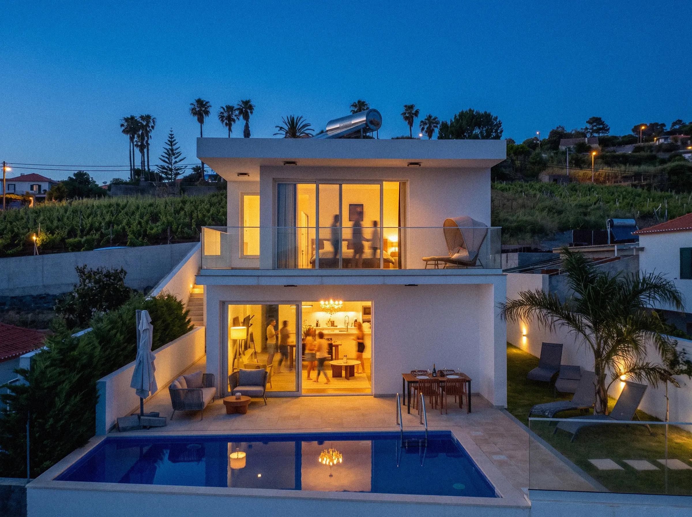 A white villa with a lit pool above the vineyards in Madeira at dusk
